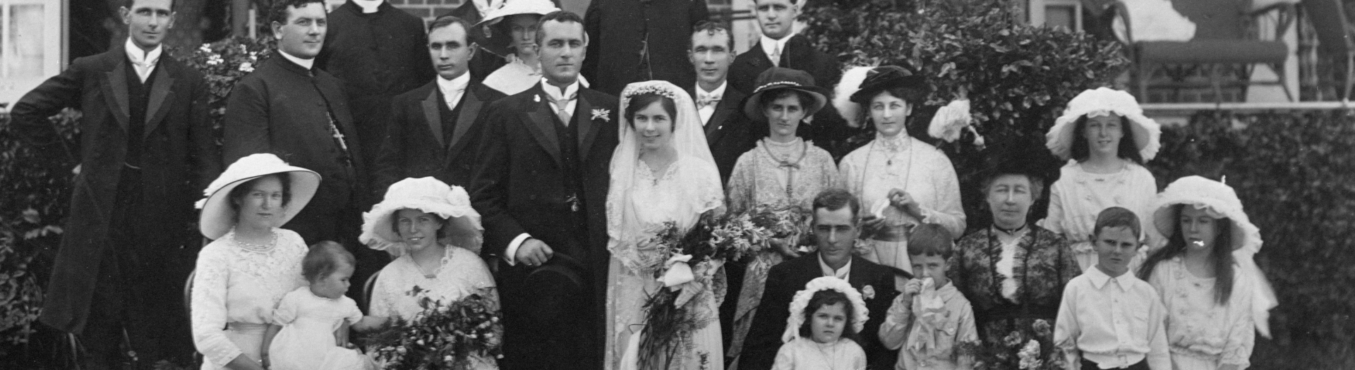 Group of men, women and children, including a bride and groom, dressed formally smiling